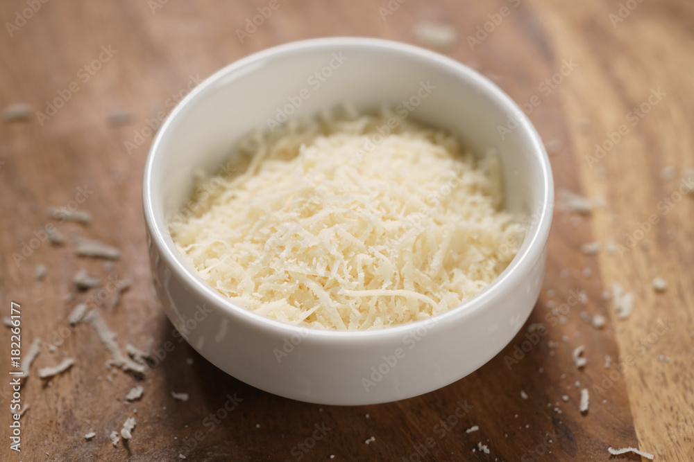 grated aged italian parmesan cheese in white bowl on table grated aged italian parmesan cheese in white bowl on table