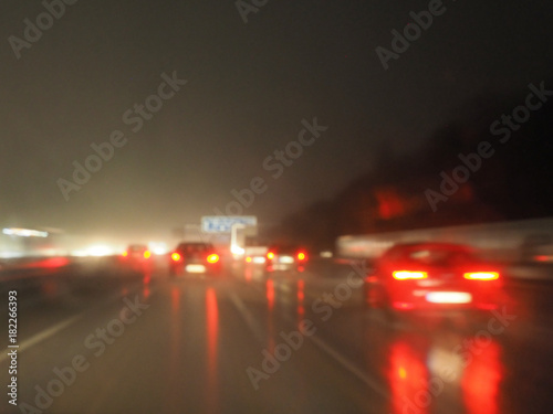 Starker Verkehr auf der Autobahn bei Nacht und Regen: Regennasse Frontscheibe, rote Rücklichter, Lichtreflexe