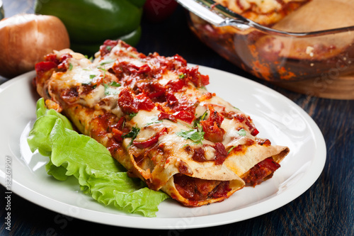 Traditional mexican enchiladas with chicken meat, spicy tomato sauce and cheese on a plate