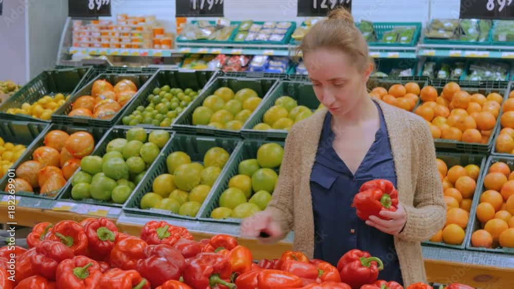 Woman buying vegetables - fresh red bell peppers at supermarket. Consumerism, sale, organic and health care concept Woman buying vegetables - fresh red bell peppers at supermarket. Consumerism, sale, organic and health care concept