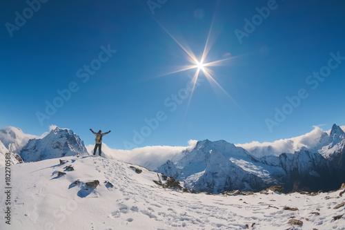 A landscape in the high Caucasus mountains with a tourist guy on top of the wide-open hands of neighboring peaks and the bright sun