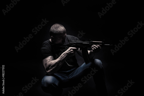 portrait of a handsome male bodybuilder, on a black background isolated, with an automatic weapon, an assault rifle in his hands. The concept of a photo of sport,