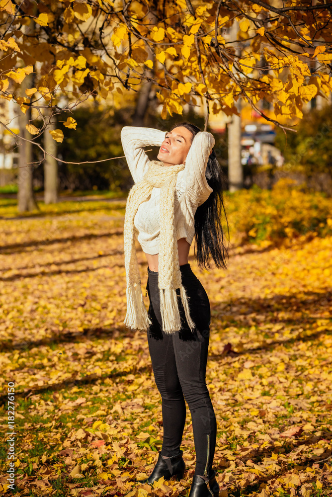 Fototapeta premium portrait of a beautiful young girl in fashionable business clothes walking along the autumn park, catching the falling leaves