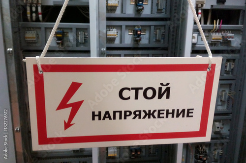 White prohibiting sign "Stop, voltage" against the background of electrical equipment. Translation of the inscription from the Russian language.