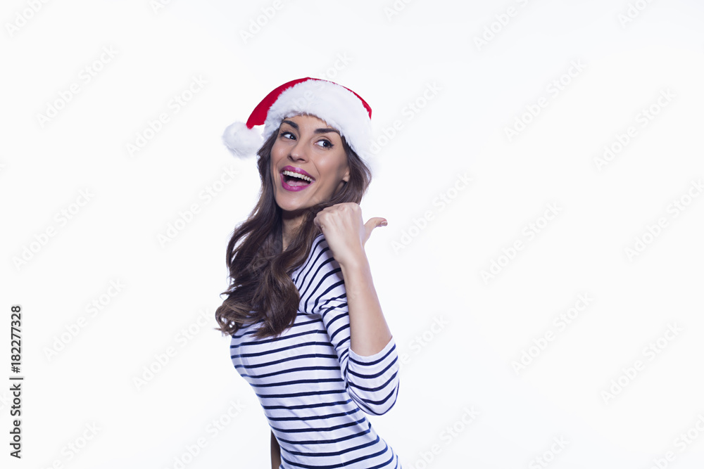 Happy New Year. Beautiful young smiling woman in santa hat posing and showing a finger at the advertising zone on a white background isolated. Happy New Year. Beautiful young smiling woman in santa hat posing and showing a finger at the advertising zone on a white background isolated.
