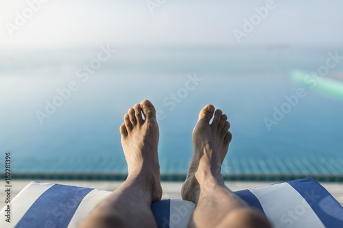 Obraz na plátne Horizontal orientation of male feet on a sun lounger overlooking an infinity poo