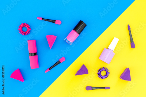 Bright decorative cosmetics. Pink and lilac nail polish and lipstick on blue and yellow background top view