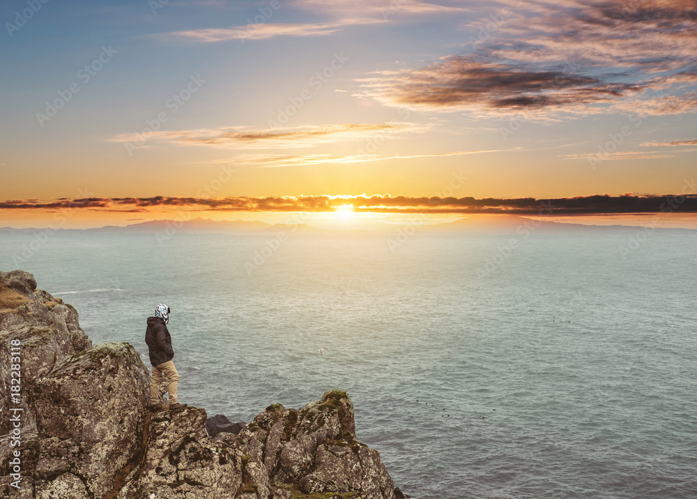 a Man standing alone on cliff, in sunset