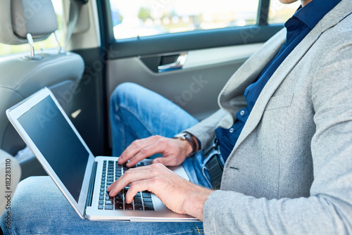 Side view closeup of successful businessman using laptop in back seat of luxury car while working with internet
