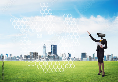 Camera headed woman standing on green grass against modern cityscape