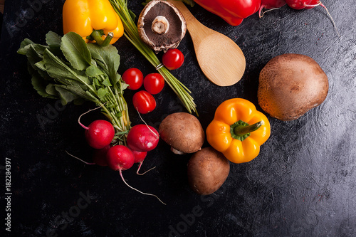 Over top close up view of different vegetables on dark table. Radish, mushrooms, green and yellow pepper on dark background