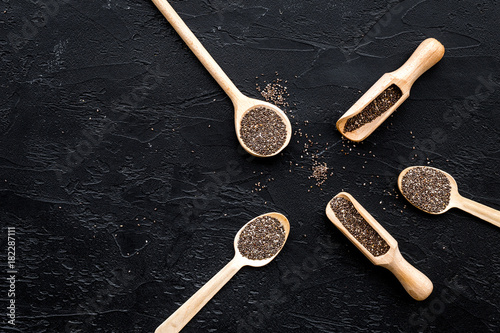 Superfood chia seeds in a wooden spoon and scoop on black background top view copyspace