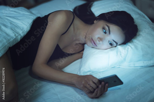 Girl is in a dark room in bed. She looks at the smartphone. Influence of social networks on youth.