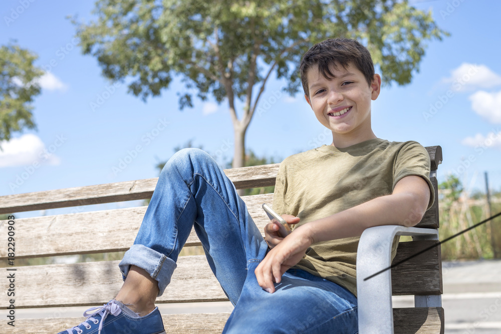 Smile schoolboy on bench taking break using mobile Smile schoolboy on bench taking break using mobile
