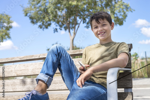 Smile schoolboy on bench taking break using mobile