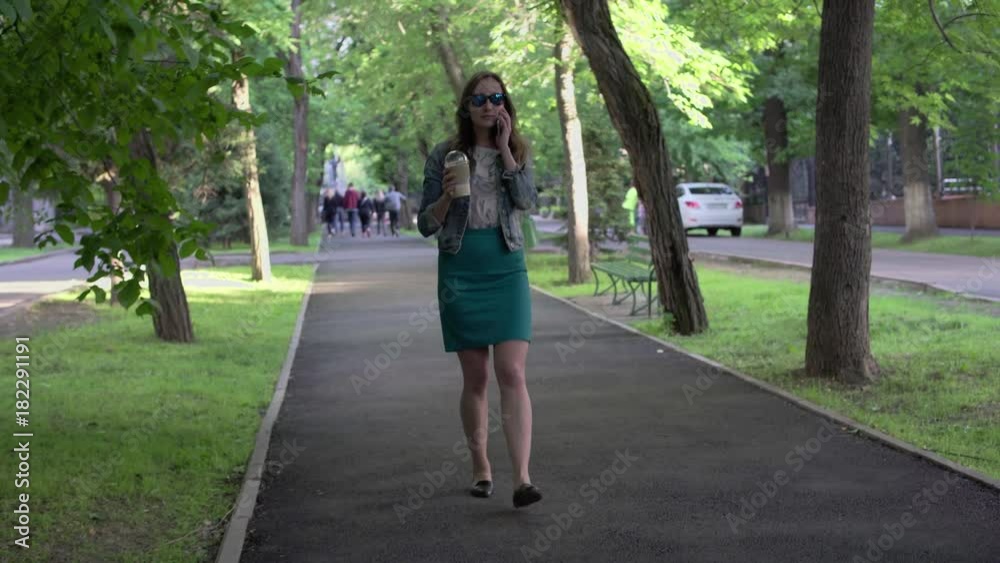 Woman talking on the phone, drinking coffee, tea with ice, drinking. Woman walking in the park and talking on the mobile phone. Woman talking on the phone, drinking coffee, tea with ice, drinking. Woman walking in the park and talking on the mobile phone.