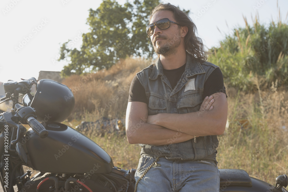 Long-haired brunette guy posing on a black custom motorcycle