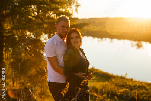 Young loving married couple on the river bank, man and beautiful girl on nature in summer