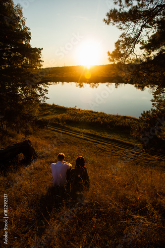 Young loving married couple on the river bank, man and beautiful girl on nature in summer