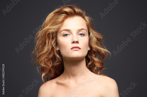 Portrait of beautiful young woman with long hair on grey background