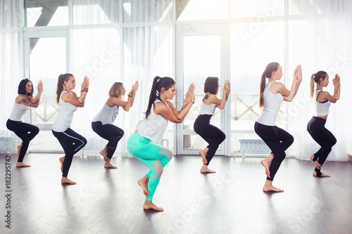 Fototapeta Naklejka Na Ścianę i Meble -  Group of young woman doing yoga Utkatasana pose indoors