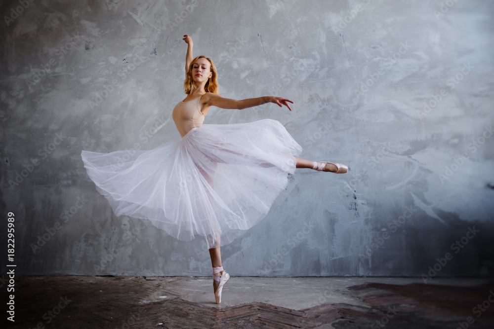 Young and slim ballet dancer is posing in a stylish studio with big windows Young and slim ballet dancer is posing in a stylish studio with big windows
