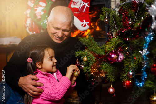 Happy family exchanging christmas gifts in decorated living room with xmas tree and fireplace. Happy loving grandfather , granddaughter and Christmas tree