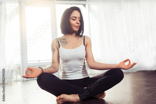 Young woman meditates while practicing yoga in Lotus pose. Freedom calmness and relax concept at home near a window, namaste