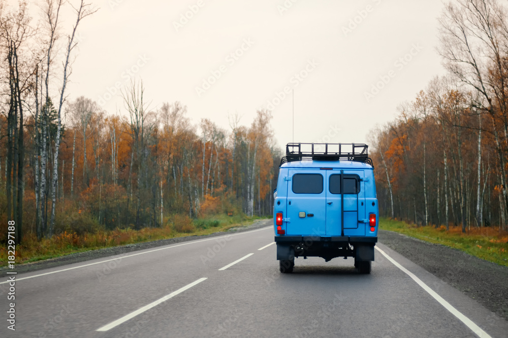 A blue van driving on a road along the forest