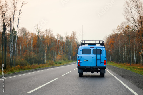 A blue van driving on a road along the forest