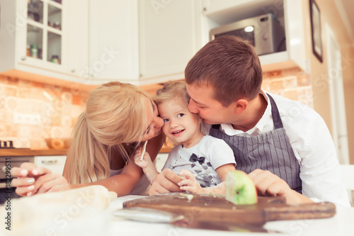 Young parents and their beautiful and cute child girl cooking and eating breakfast ot lunch at kitchen table at home