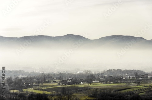 foggy rural landscape of village with green fields and mountains hill top