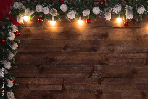 New Year's background with the texture of wooden boards, a corner of fir branches with red balls and burning lights.