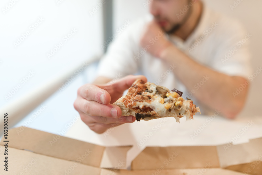 A man holds a piece of pizza in his hands. The man eats a pizza. Focus on a piece of pizza.