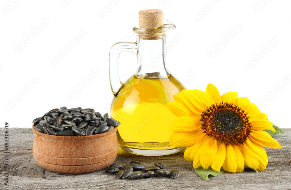 Sunflower oil in glass jug , seeds and flower on old wooden table with white background Sunflower oil in glass jug , seeds and flower on old wooden table with white background