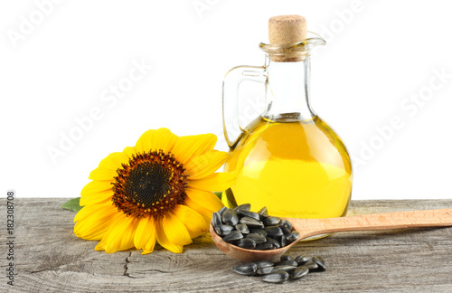 Sunflower oil in glass jug , seeds and flower on old wooden table with white background