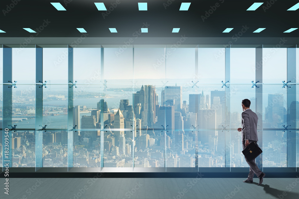 Businessman in front of office window thinking of new challenges Businessman in front of office window thinking of new challenges
