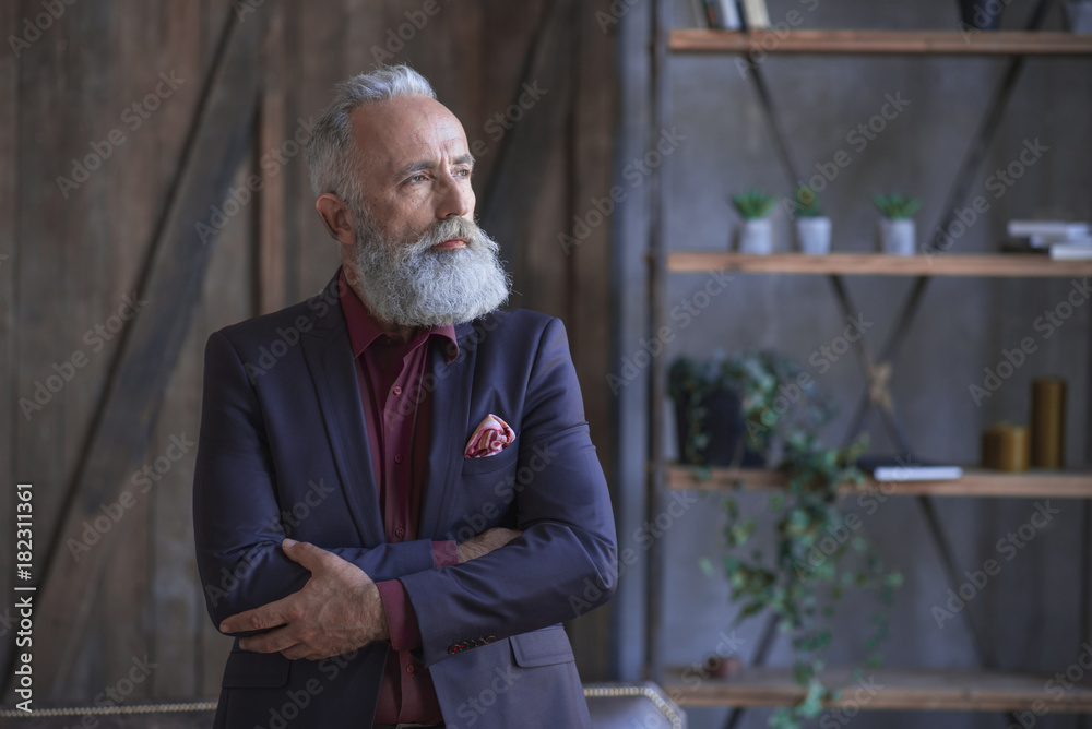 Portrait of serene unshaven old businessman with crossing arms locating indoor. Work concept Portrait of serene unshaven old businessman with crossing arms locating indoor. Work concept