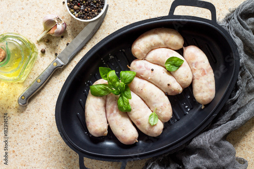 Raw homemade sausages on slate background, with basil and spices.