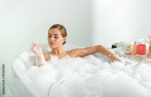 Confident girl is taking a bath with bubbles. She is looking at her clear hand with satisfaction. Luxury concept