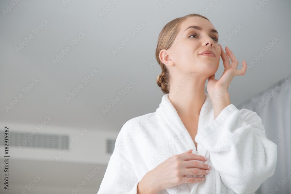 Low angle of pretty young woman is satisfied with her skin. She is touching face and smiling while standing in bathrobe. Copy space Low angle of pretty young woman is satisfied with her skin. She is touching face and smiling while standing in bathrobe. Copy space
