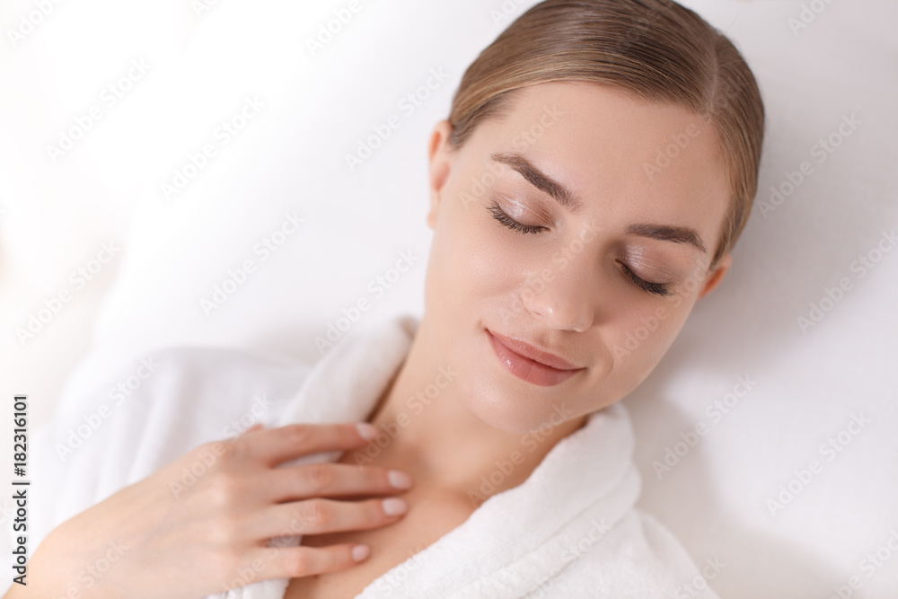 Portrait of cute young woman enjoying peace and comfort at beauty salon. She is lying on deckchair in white bathrobe Portrait of cute young woman enjoying peace and comfort at beauty salon. She is lying on deckchair in white bathrobe