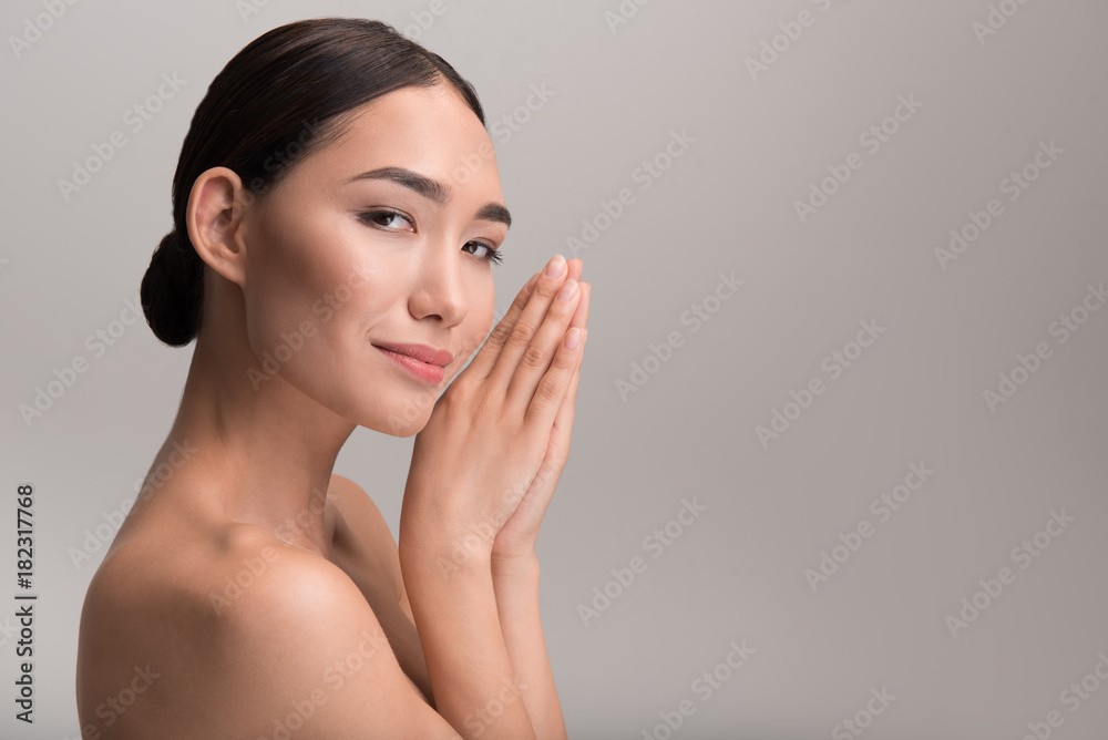 Tenderness. Side view of charming young naked asian woman with healthy complexion. She is looking at camera with slight smile while folded her palms together. Isolated and copy space in right side