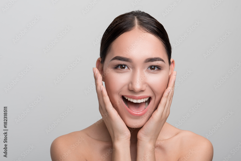 Sense of admiration. Portrait of cheerful naked young asian girl is touching her face while expressing happiness. She is looking at camera with wide smile while standing isolated. Skincare concept Sense of admiration. Portrait of cheerful naked young asian girl is touching her face while expressing happiness. She is looking at camera with wide smile while standing isolated. Skincare concept