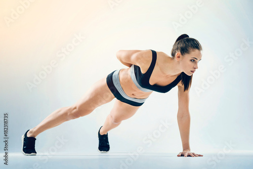 Beneficial activity. Confident fitness lady in a navy blue sportswear doing a one arm push up with one hand on the floor and the other hand behind her back during an intensive training session.