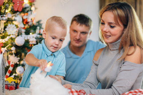 Young happy family of three playing near christmas tree. Mother and father having fun with son in living room. Happy parenting concept. New Year's interior