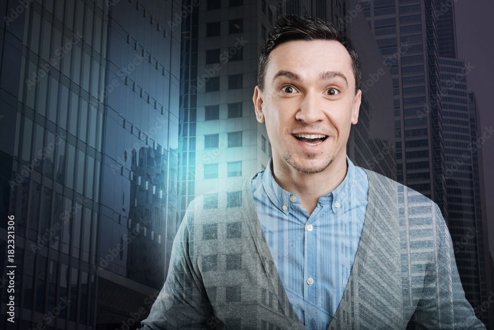 Cannot keep my emotions inside. Extremely happy millennial guy looking into the camera with his eyes and mouth wide opened while getting excited over something.