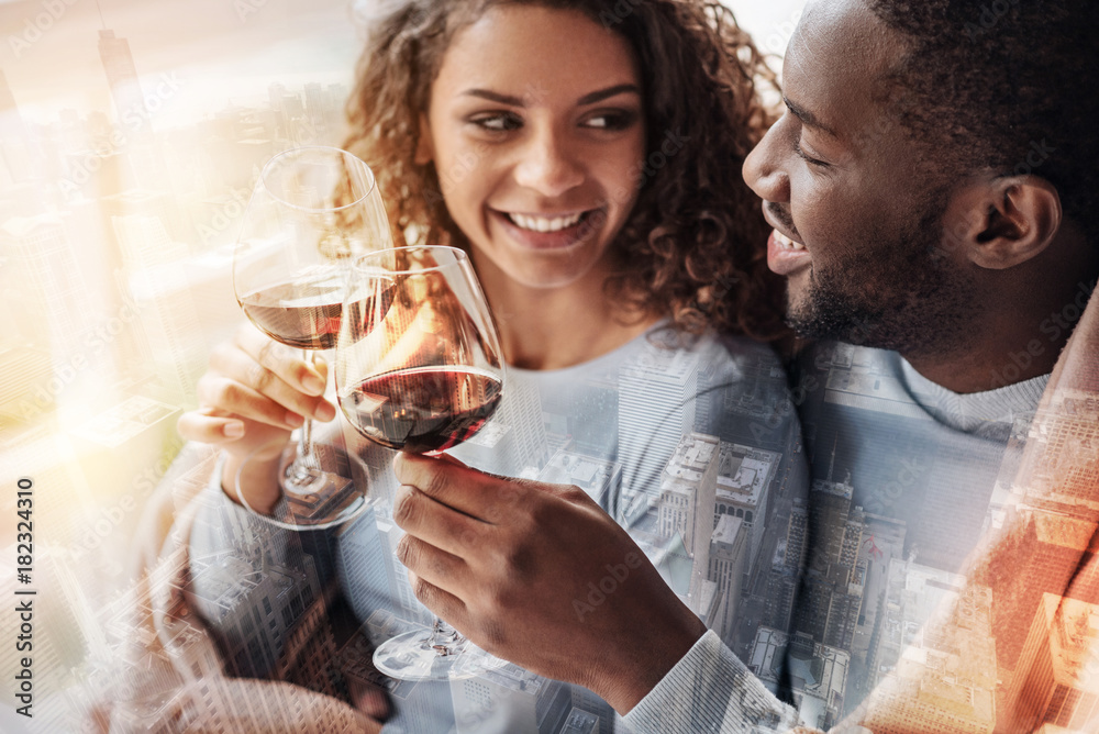 Happiness in eyes. Close up of young pleasant couple sitting close to each other while holding glasses with wine and expressing delight Happiness in eyes. Close up of young pleasant couple sitting close to each other while holding glasses with wine and expressing delight