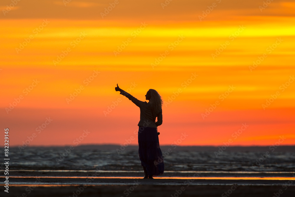 Feeling positive, winning, success, achieving life goals, life is good, positive mood.  Silhouette beautiful smiling woman thumb up on the sunset/Girl enjoys the beautiful sunset / Meet a new day