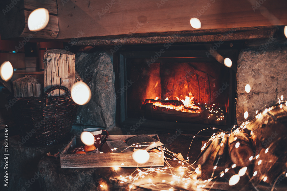 Warm cozy fireplace with real wood burning in it. Magical atmosphere. Cup  of hot drink and